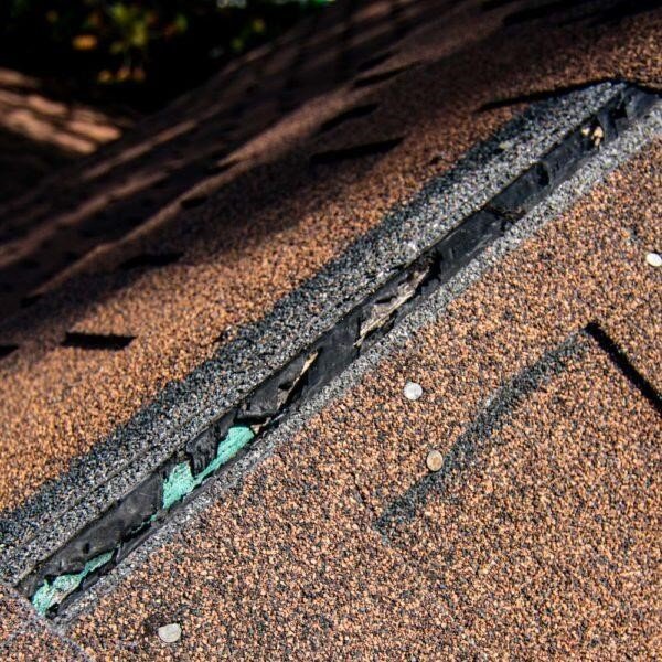 Identifying structural wind damage and lifted shingles on a residential roof peak.