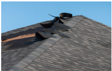 Clear signs of storm and wind damage on residential asphalt roof shingles.