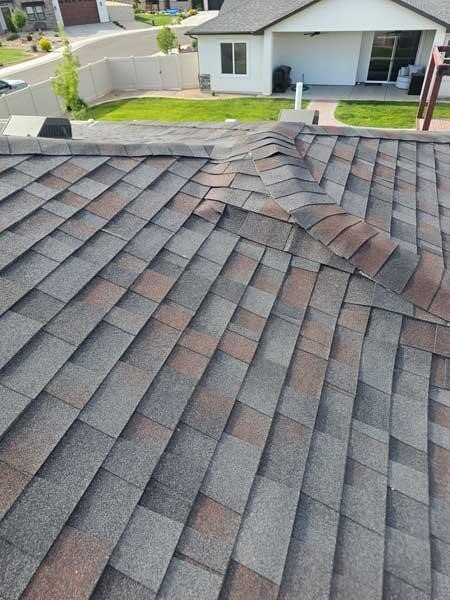 Severe roof damage featuring buckled asphalt shingles in need of professional repair.