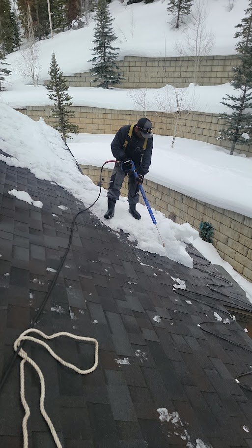 Worker clearing snow from a shingle roof.