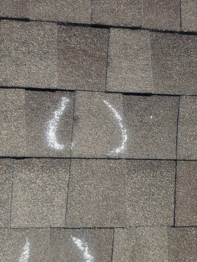 Close-up of asphalt shingles with a circled impact mark.