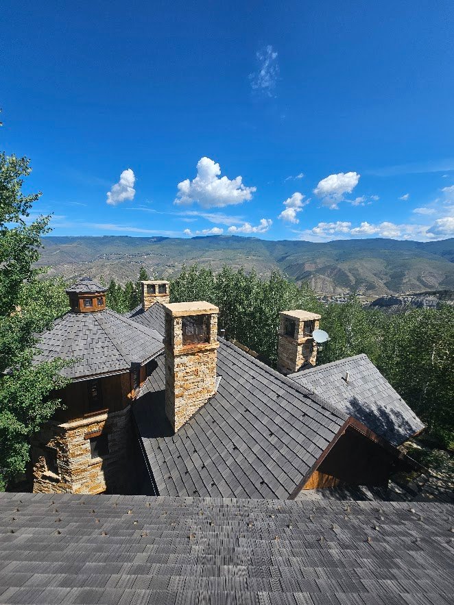 Custom residential roof replacement with grey shingles and stone chimneys on a luxury mountain home.